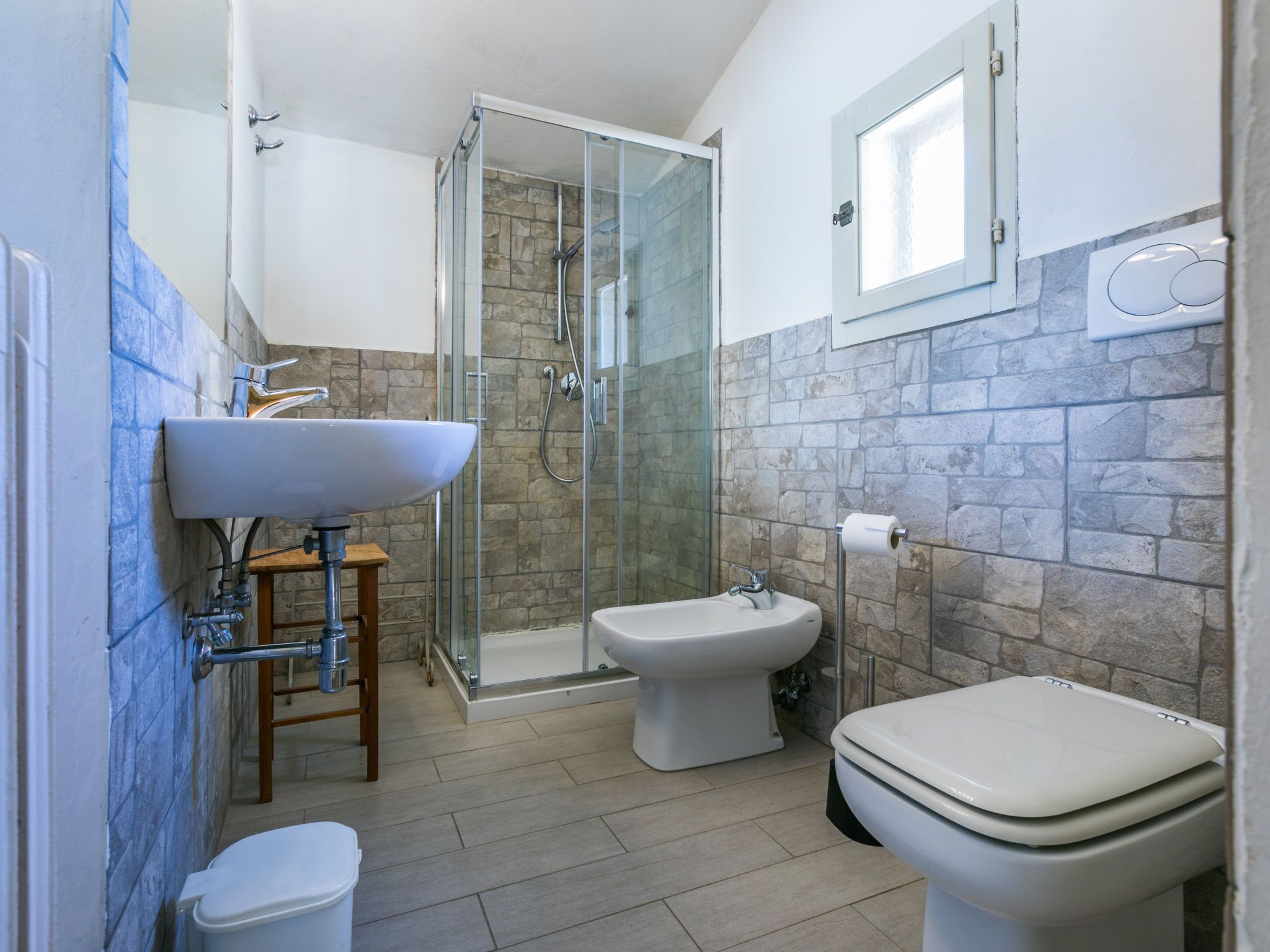 A modern bathroom with a glass-enclosed shower, a pedestal sink, a bidet, and a toilet.