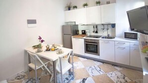 A compact kitchen with white cabinets, a built-in oven, a microwave, and a sink. There is a dining table with chairs and a small potted plant on the counter. - Bufalini 2 - Raffaello by Interhome (Florence)