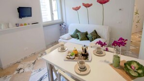 A modern room with a white sofa, a dining table set with plates, cups, and a vase of flowers. - Bufalini 2 - Raffaello by Interhome (Florence)