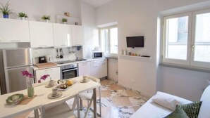 A modern kitchen with white cabinets, a dining table, and a TV mounted on the wall. - Bufalini 2 - Raffaello by Interhome (Florence)