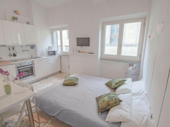 A compact, well-lit room with a bed, a desk, and a kitchenette.