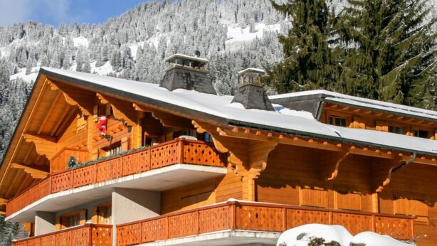 Een houten chalet met balkon, met een besneeuwde berg op de achtergrond.