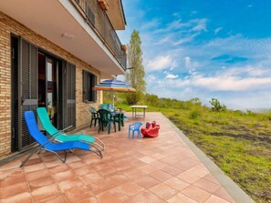 A patio with two blue lounge chairs, a table with chairs, a colorful umbrella, and a red boat toy. - Vacation home Elena by Interhome (Mascali)