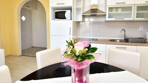 Een moderne keuken met witte kasten, een magnetron en een RVS spoelbak. Op de eettafel staat een vaas met bloemen.
