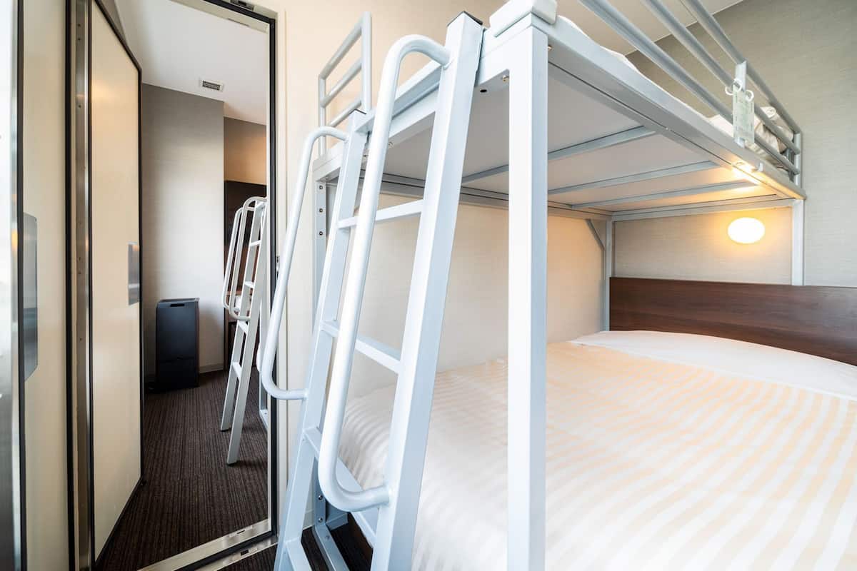 A bunk bed room with a wooden headboard, a bedside table, and a wall-mounted light.