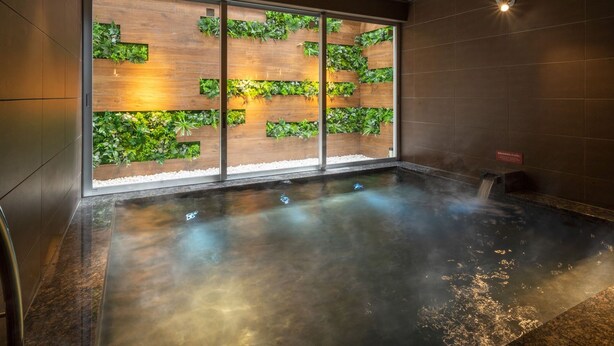 A spa area with a heated stone bath, wooden panel walls with greenery, and a tiled floor. - Super Hotel Ehime Ozu Inter (Ozu)