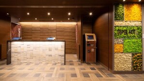 A reception area with a check-in counter, a self-service kiosk, and a wall with vertical garden panels. - Super Hotel Ehime Ozu Inter (Ozu)