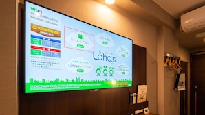 A hotel room with a large screen displaying a WiFi network name, SSID, and password. - Super Hotel Ehime Ozu Inter (Ozu)