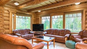 Interior d'una cabana de fusta amb sofàs de pell, televisió de pantalla plana i finestres grans que donen a una vista del bosc.