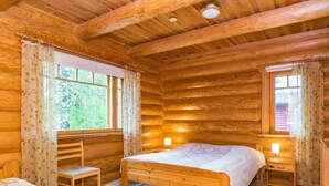 Un dormitori de cabana de fusta amb un llit, una cadira i dues taules de nit amb làmpades.