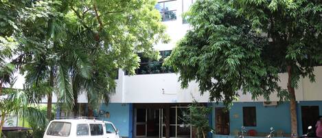 Un edificio de fachada blanca y azul, una camioneta estacionada adelante y varias motocicletas afuera.