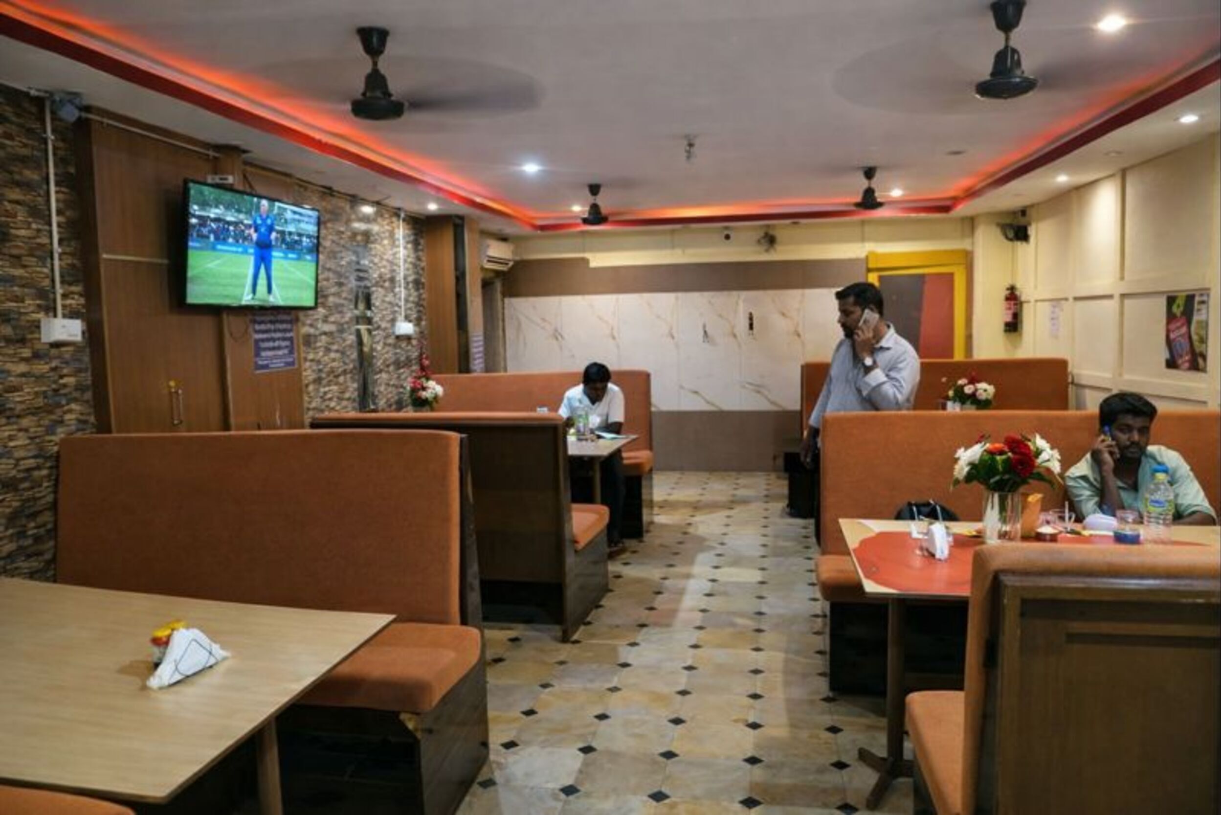 Un restaurante con cabinas y mesas, una pantalla de televisión en la pared y un suelo con diseño.