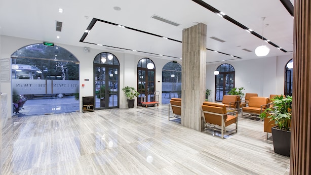A spacious lobby with a marble floor, large arched windows, and orange seating areas. - The Twin Hotel (Bai Chay)