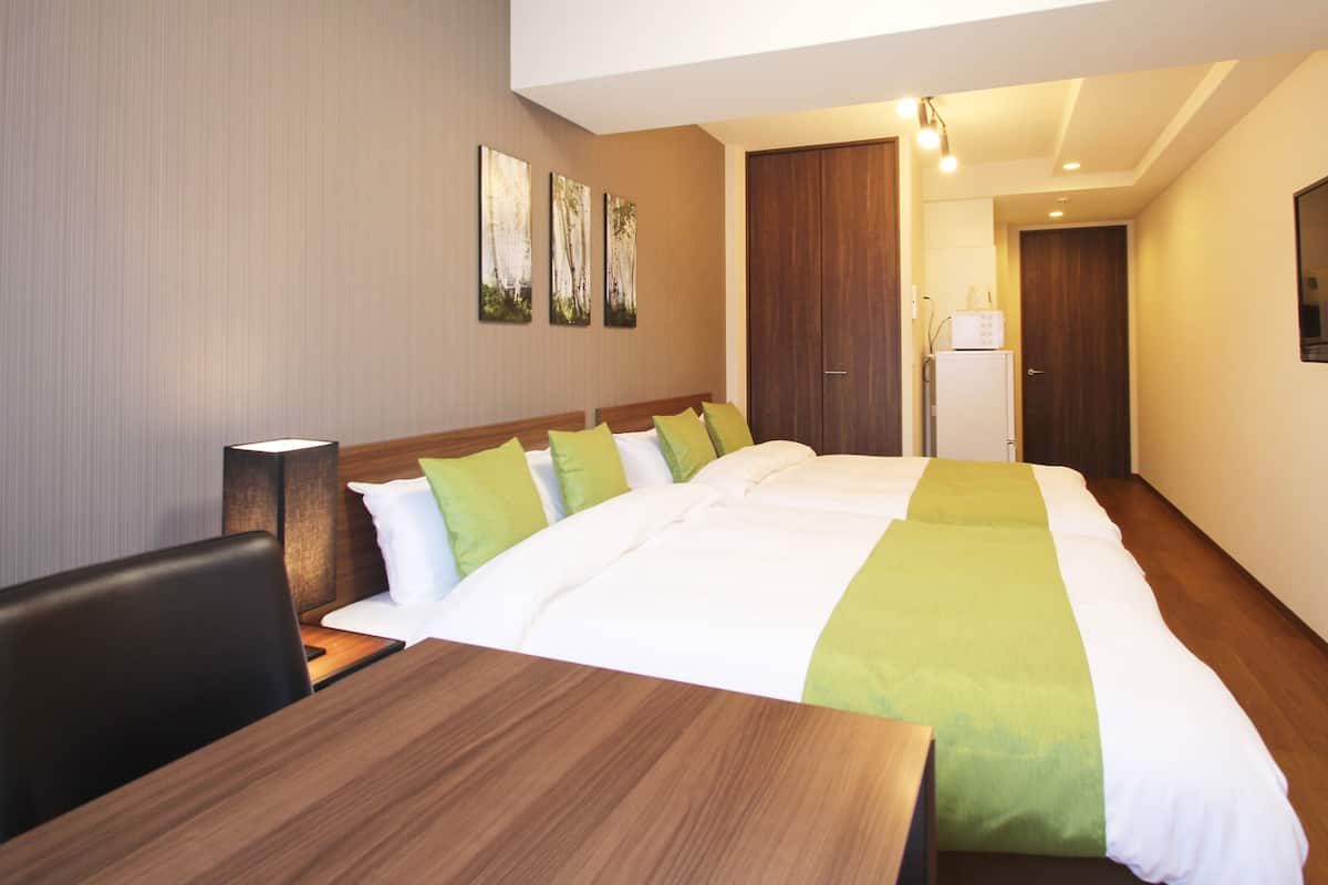 Habitación de hotel con una cama grande, un escritorio de madera, una silla, un televisor de pantalla plana montado en la pared y una puerta que da a otra habitación.