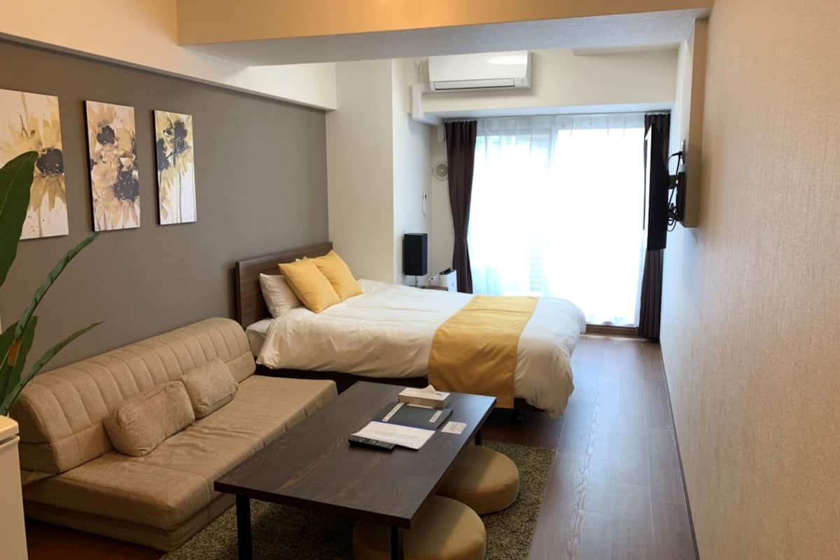 Una habitación de hotel moderna con un sofá, una cama con detalles en amarillo, una mesita de centro y obras de arte en la pared.