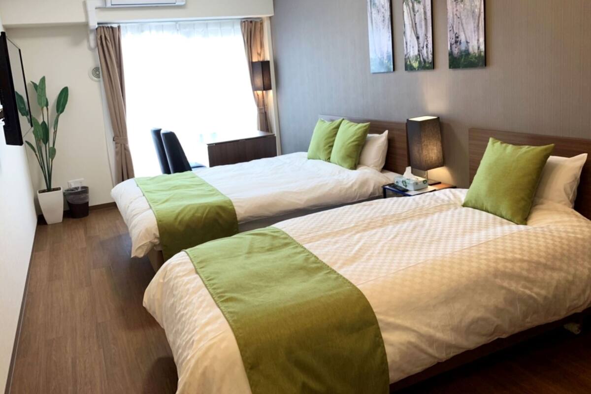 Habitación de hotel con dos camas, una planta en maceta, un escritorio y una ventana con cortinas.