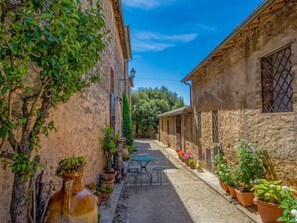 A narrow alley with stone buildings, a table and chairs, and potted plants.