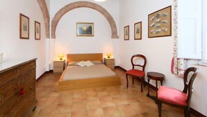 Ein Schlafzimmer mit einem Bett, zwei Nachttischen, einem Schminktisch, einem Sessel und einem kleinen Tisch.
