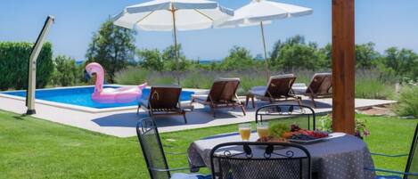 Un espace aménagé au bord de la piscine, avec des chaises longues, des parasols et une table où sont disposés des fruits et des boissons.
