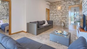 A modern living room with a stone wall, a grey sofa, a coffee table with a plate of food, and a television. - Vacation home Blog 2 by Interhome (Poreč/Sv. Lovreč)