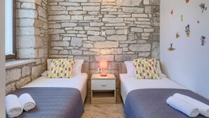 A room with two beds, each with a colorful pillow, a nightstand with a lamp, and an air conditioning unit on the stone wall. - Vacation home Blog 2 by Interhome (Poreč/Sv. Lovreč)
