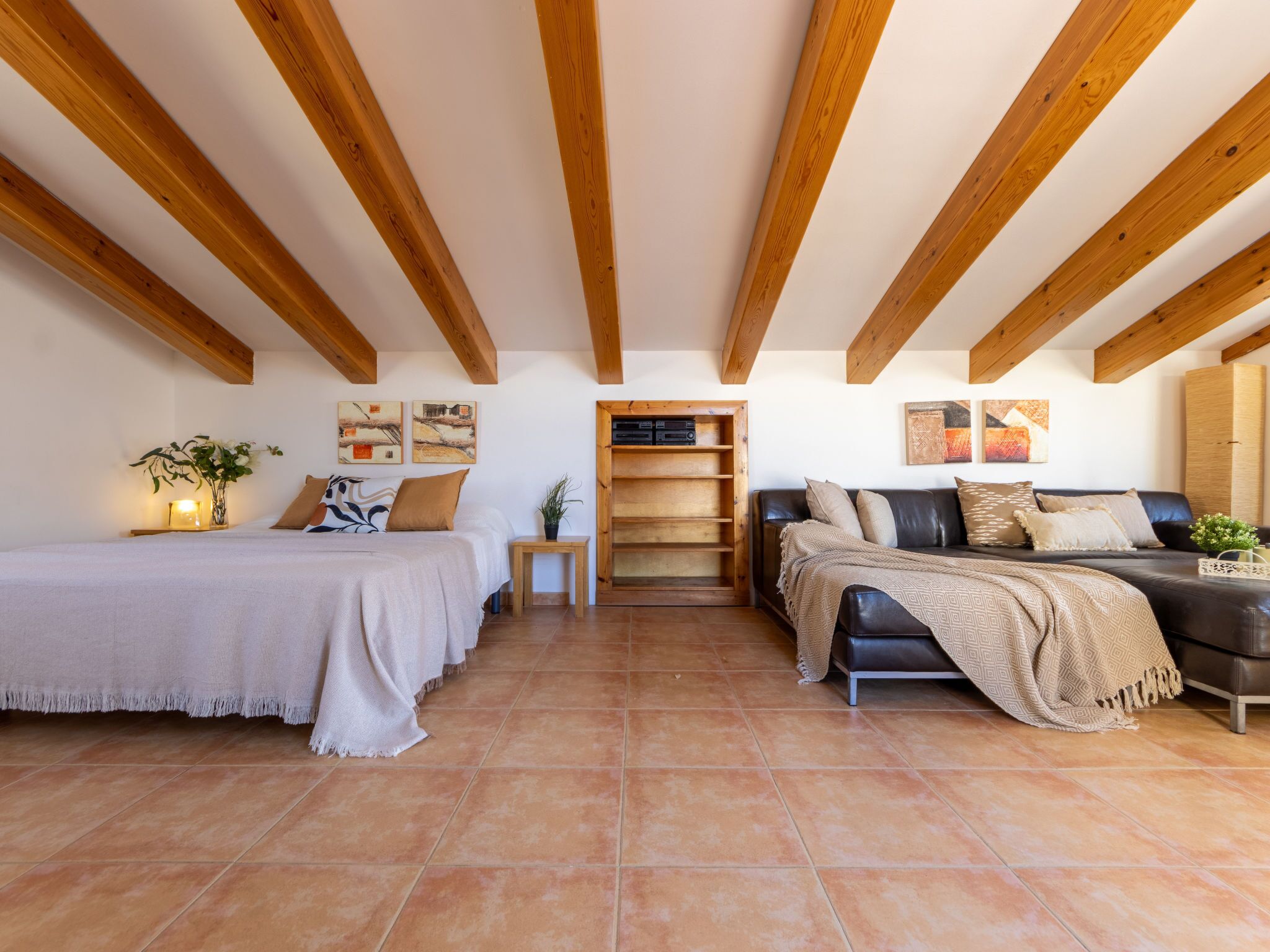 A spacious room with a bed, a sofa, and a wooden bookshelf.