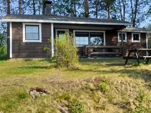 Une maison de plain-pied avec un porche à l’avant, une cheminée et un petit jardin agrémenté d’un banc en bois.