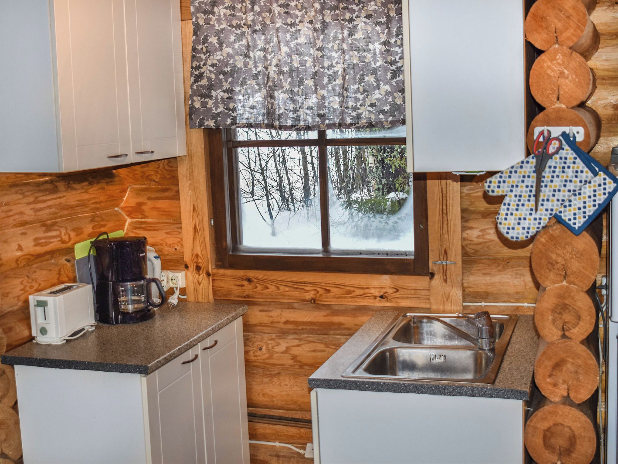 Une cuisine de style rustique, avec une fenêtre, des murs en bois, un évier et des appareils électroménagers de base.