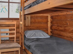 Un lit superposé en bois avec un matelas et un oreiller gris, une chaise en bois et une petite armoire en bois.