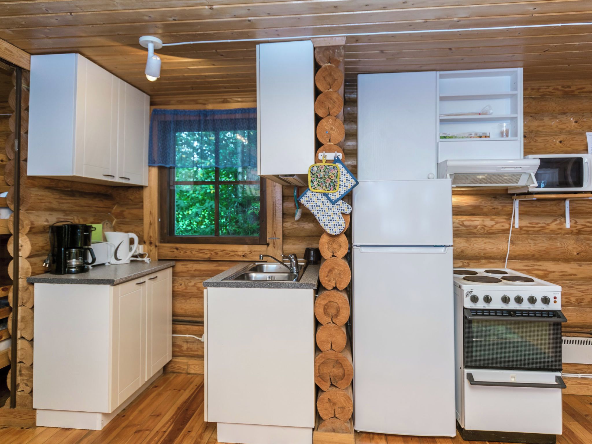A compact kitchen with white cabinetry, a refrigerator, a stove, and a microwave.