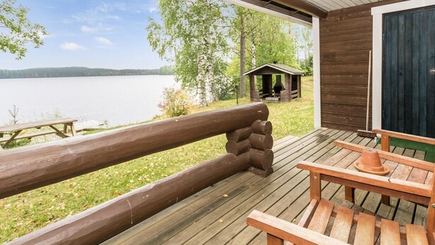 Una terraza de madera con vista a un lago, una mesa de picnic y una pequeña construcción de madera.