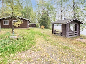 A cabin with a small shed and a fenced area, surrounded by trees and a body of water.