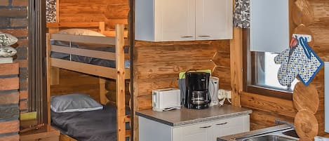 A compact room with a bunk bed, kitchenette, and a small stool.