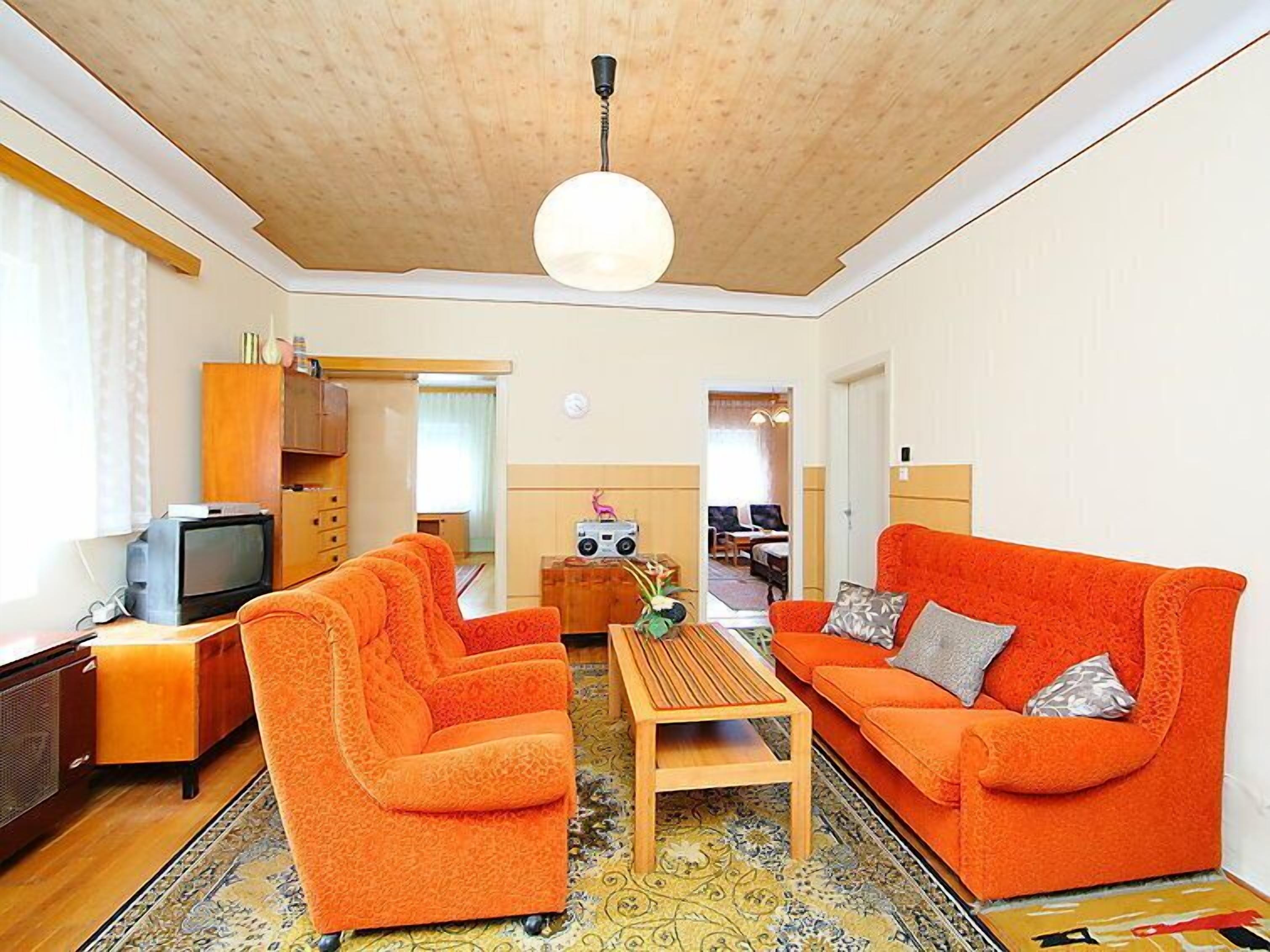Un salon avec deux canapés orange, une table basse en bois, un téléviseur et un luminaire au plafond.