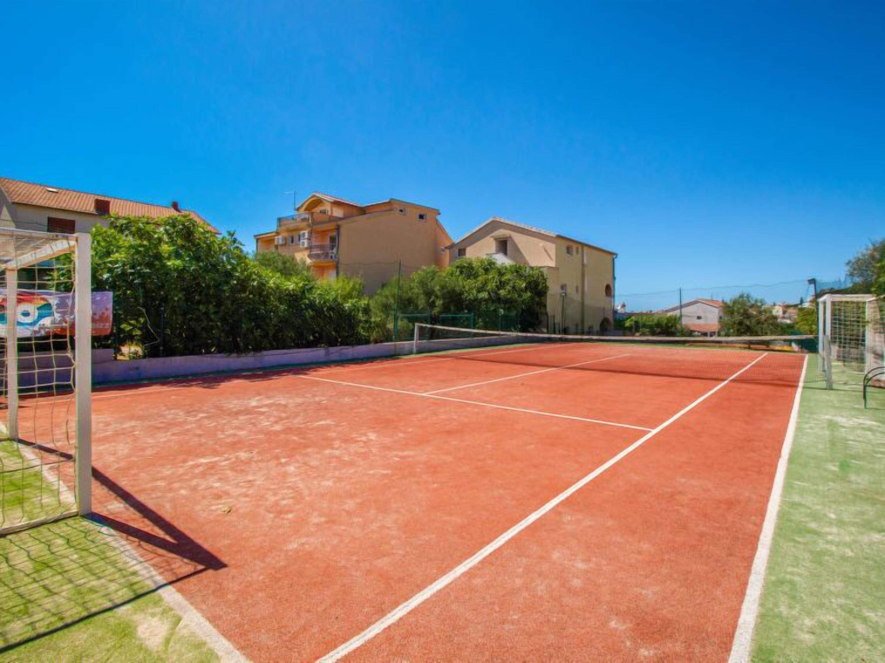 A tennis court with a net, surrounded by greenery and buildings.