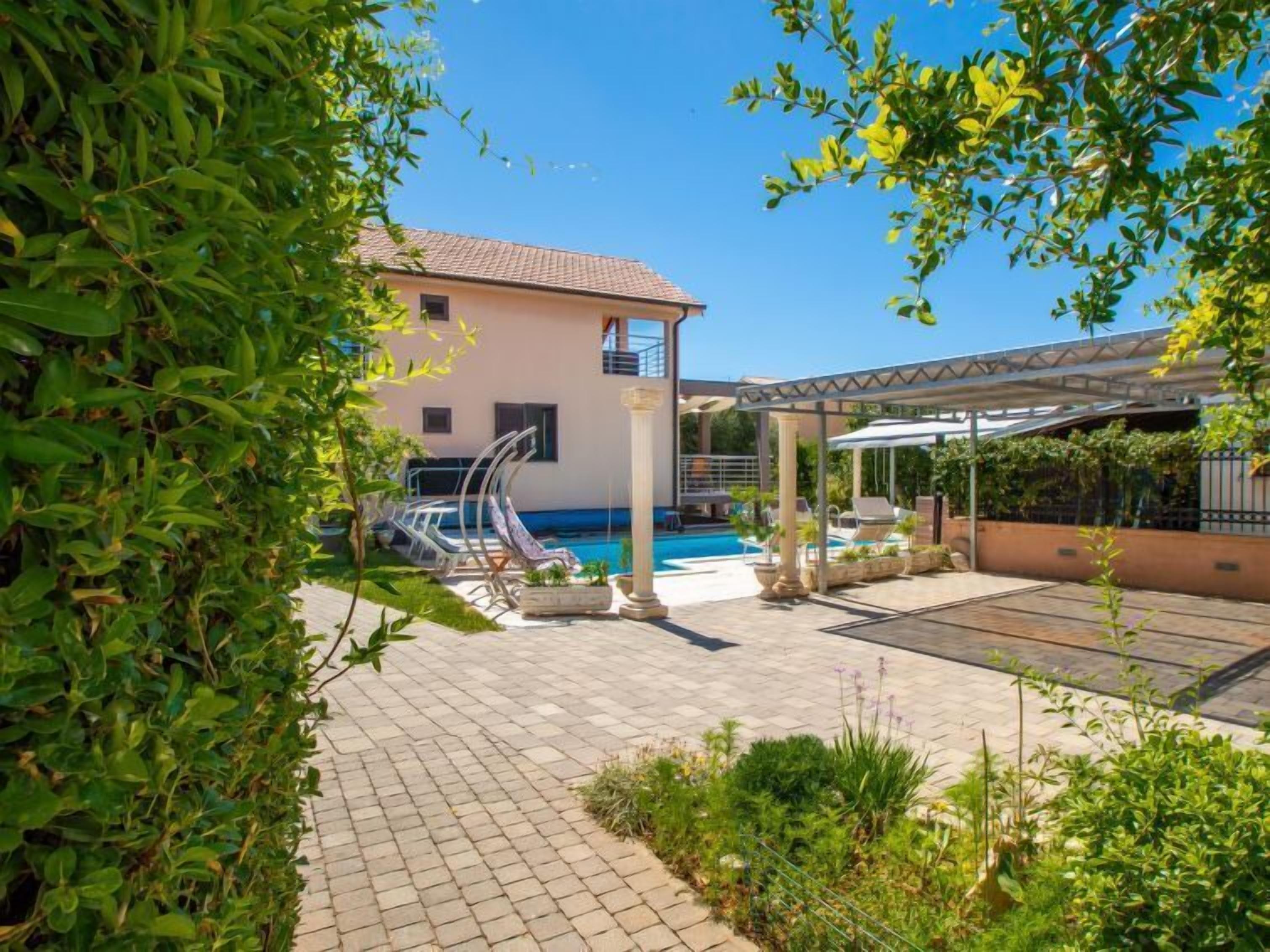A pool area with a clear blue pool, lounge chairs, and a covered seating area.