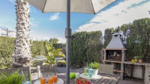 An outdoor patio with a wooden table set for a meal, a grill, and potted plants. - Miramar by Interhome (Deltebre)