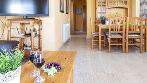 A living room with a TV, wooden furniture, a dining table with chairs, and a potted plant. - Miramar by Interhome (Deltebre)