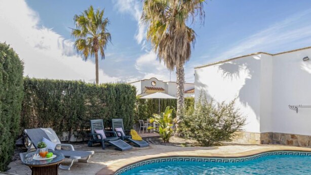 A pool area with lounge chairs, a table with drinks, and a white wall with a decorative design. - Miramar by Interhome (Deltebre)