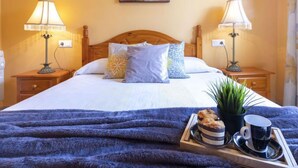 A neatly made bed with a blue blanket, two bedside lamps, a floral painting on the wall, and a tray with pastries and a cup on the bed. - Miramar by Interhome (Deltebre)