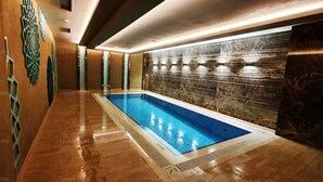 Piscina interior moderna com parede revestida de azulejos e chão de madeira.
