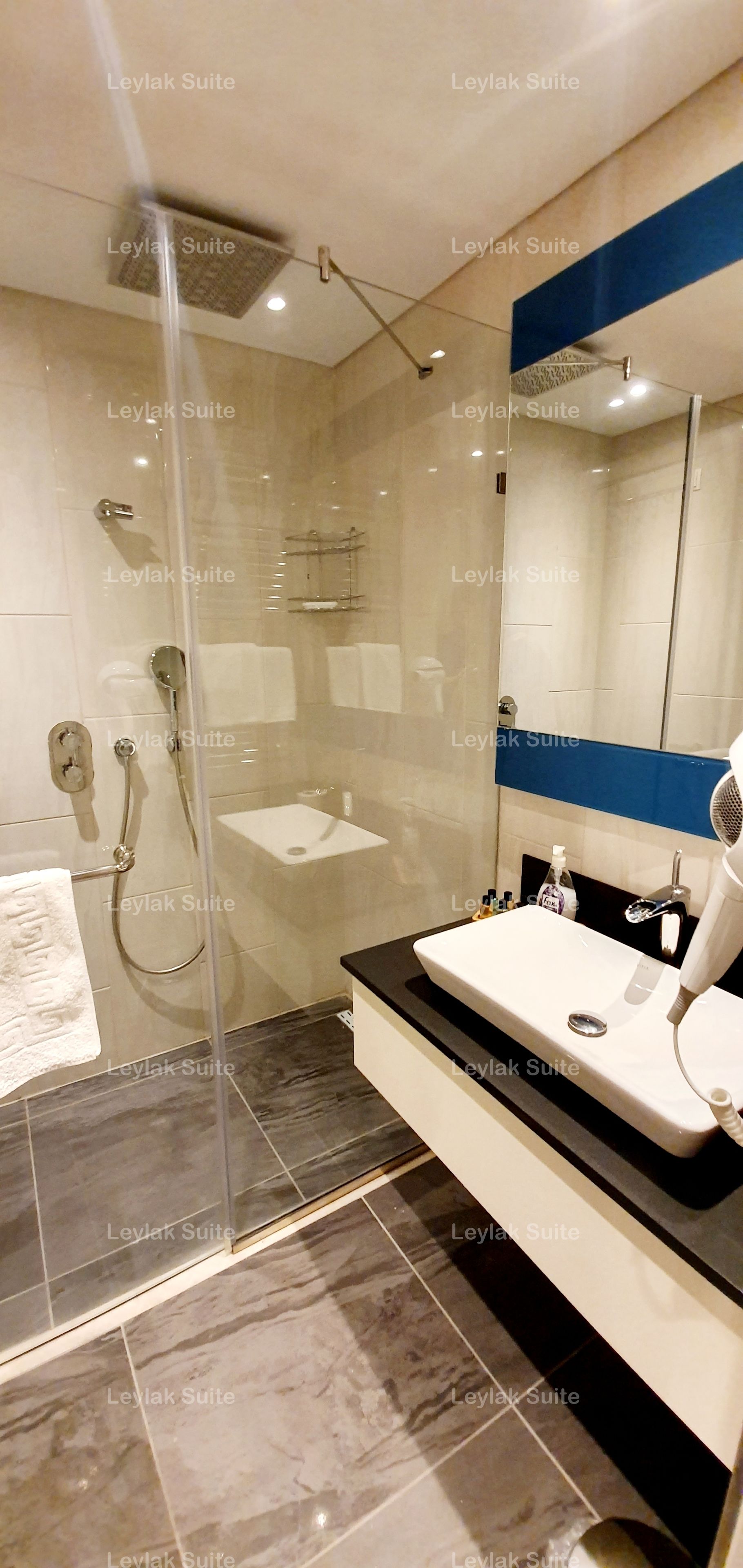 Ein modernes Badezimmer mit einer begehbaren Glasdusche, einem weißen Waschbecken und einem Waschtisch mit Spiegel.