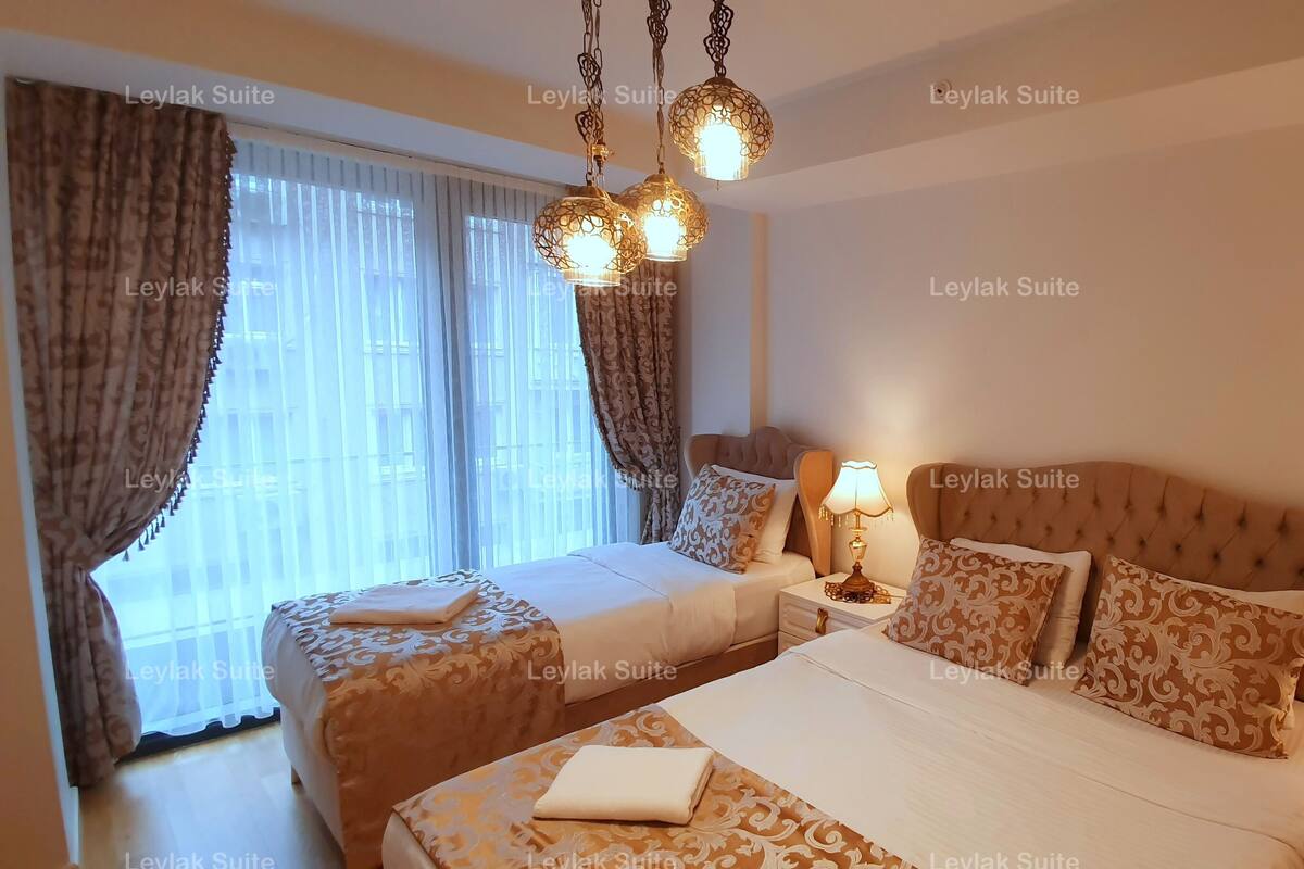 A hotel room with two beds, patterned bedding, a chandelier, and a nightstand with a lamp.