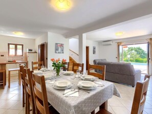 Un coin repas avec une table dressée pour quatre personnes, une cuisine en arrière-plan et un canapé gris dans l’espace salon.