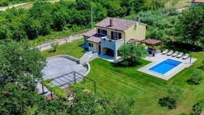 Et toetagers hus med en stensokkel, swimmingpool og en terrasse med liggestole.