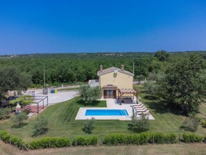 Une maison de plain-pied avec une piscine, entourée d’une pelouse bien entretenue et d’arbres.