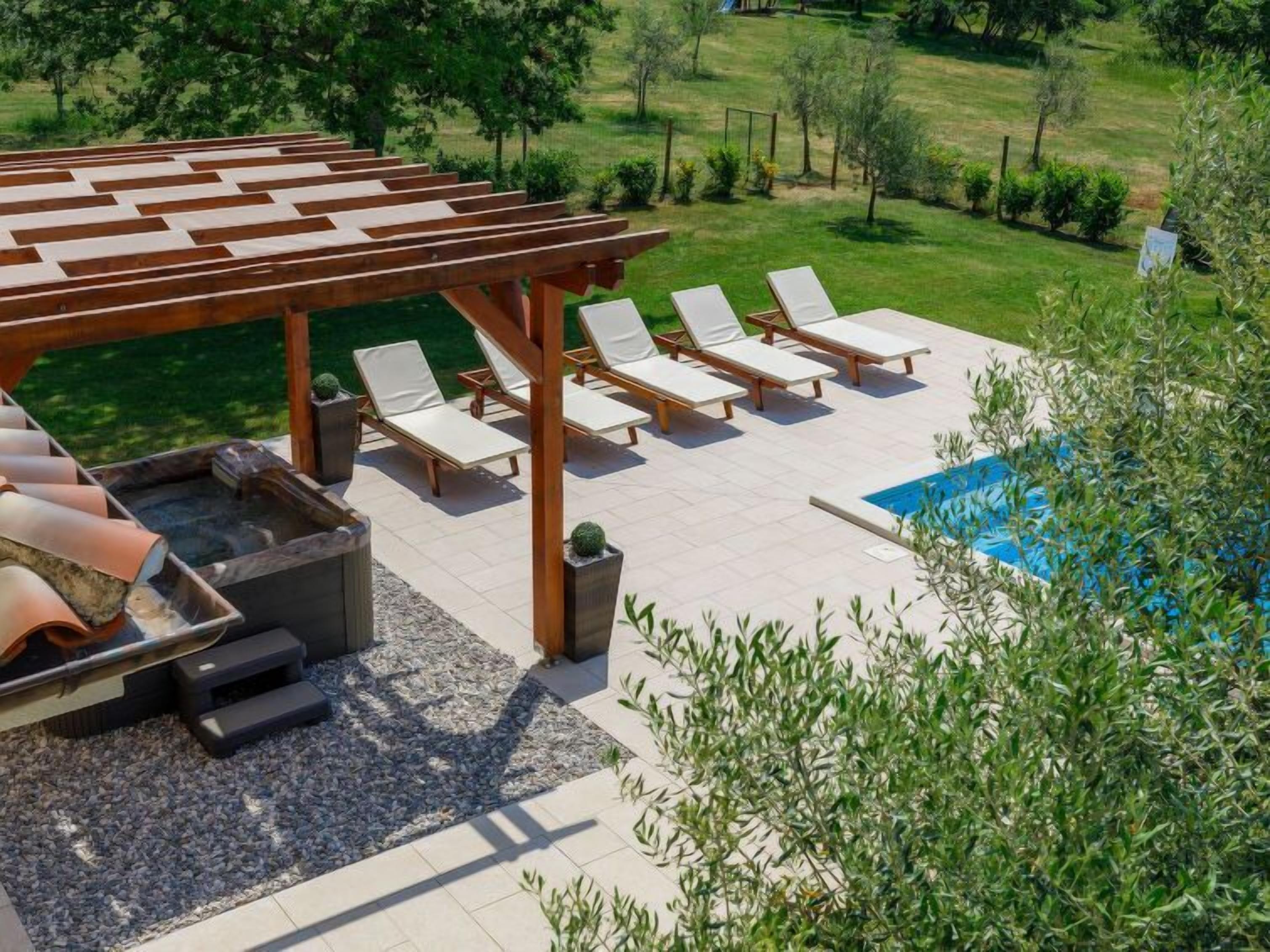 Een zwembadgedeelte met ligbedden, een pergola en een jacuzzi.