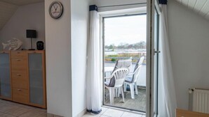 A room with a sliding glass door leading to an outdoor patio with white chairs.