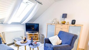 A cozy living room with a TV, blue sofa, and a dining table with candles.