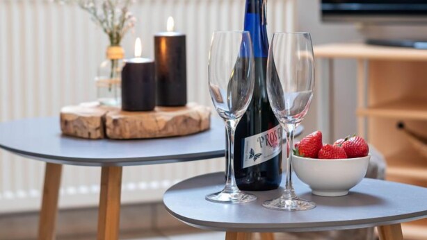 A table with a bottle of wine, two glasses, a candle, and a bowl of strawberries.